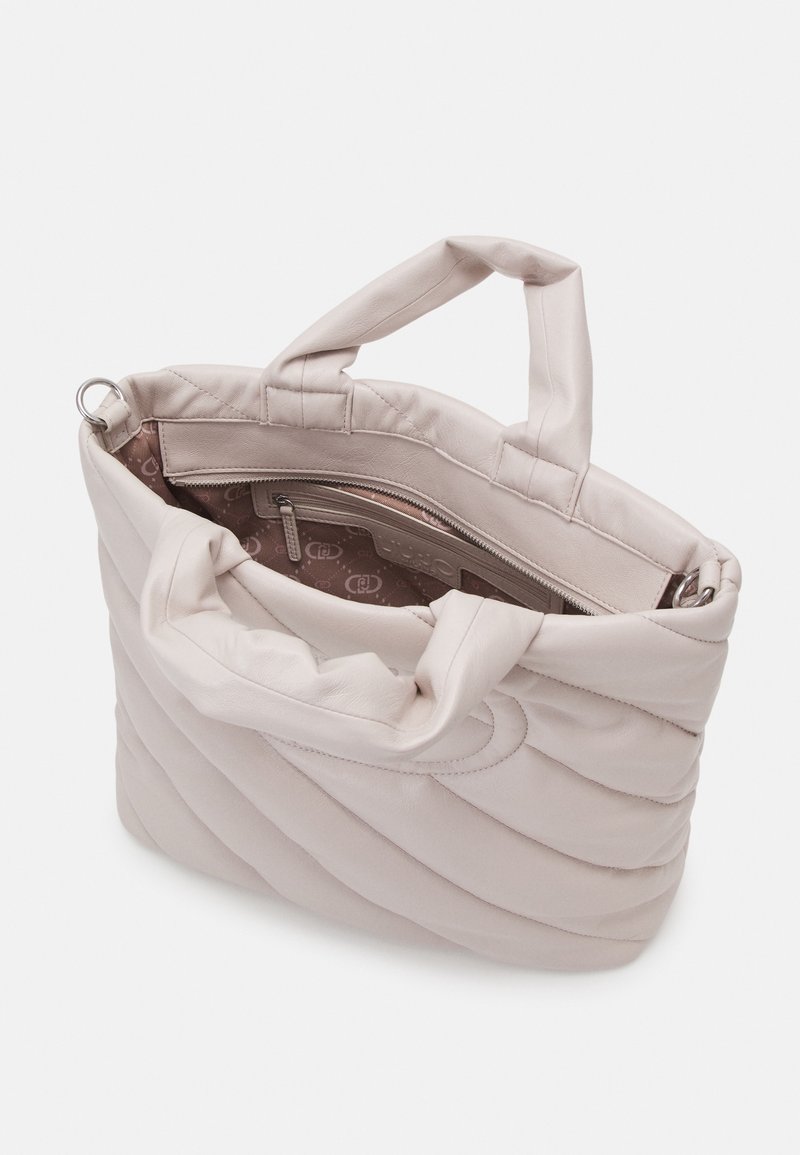 Sac à main matelassé beige clair avec deux poignées, partiellement ouvert pour montrer une poche intérieure zippée avec doublure imprimée.