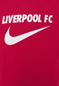 Tissu rouge avec un texte blanc indiquant "LIVERPOOL FC" au-dessus d'un grand logo Nike swoosh blanc.