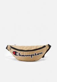 Banane en tissu beige avec des accents noirs et un grand logo "Champion" en noir et rouge. Dispose d'un compartiment zippé et d'une sangle ajustable.