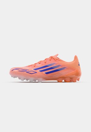 Helle orange Fußballschuhe mit blauen Streifen, einer strukturierten Oberseite und einem aerodynamischen Design. Verfügt über eine Kombination aus geformten und konischen Stollen.