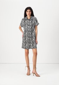 Φόρεμα μαύρου και λευκού μοτίβου με κοντά μανίκια, σφιχτή μέση και γιακά με κουμπιά. Συνδυάζεται με μπεζ σανδάλια με ψηλό τακούνι και λουράκια.