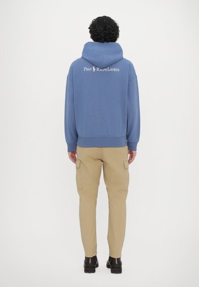 Blå hætte sweatshirt med et logo på ryggen, parret med beige cargo bukser og sorte fodtøj. Enkel design og afslappet pasform.