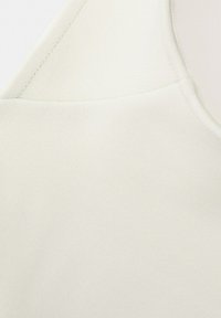 Gros plan sur un tissu blanc montrant une texture lisse et des détails de couture sur un vêtement, probablement une manche ou une zone d'épaule.