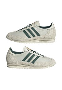 Tenisky Adidas s bielou koženou hornou časťou a zelenými akcentmi, textúrovanou krémovou semišovou špičkou a pätou a s retro siluetou.