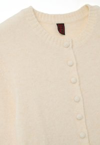 Cardigan color crema realizzato in tessuto morbido, con scollo rotondo, bordi a costine e cinque bottoni texturizzati sul davanti.