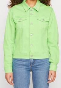 Grön denimjacka med klassisk krage, silverknappar, två bröstfickor och en figursydd siluett. Texturerat tyg, avkortad längd.