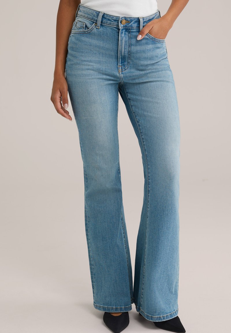 Hellblaue Schlagjeans aus Denim, mit hoher Taille, Fünf-Taschen-Design und leichter Ausbleichung, kombiniert mit schwarzen Spitzenschuhen.