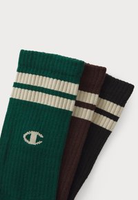 Tres pares de calcetines de tripulación en verde, marrón y negro. Cada par presenta una textura acanalada y dos rayas horizontales en crema. Logo presente en el calcetín verde.