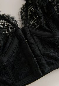 Juodas nėriniuotas braletė, puošnus gėlių raštais, tekstūruota tinklelis, satino apdaila ir kabliuko bei akių užsegimas su metaliniais akcentais.