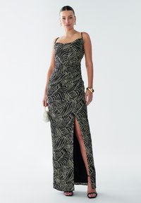 Maxi dress in black with a wavy white pattern. Features thin straps, form-fitting design, and a thigh-high slit. Smooth texture.