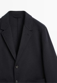Blazer en laine bleu marine foncé avec revers en encoche, deux boutons sur le devant et deux poches inférieures à rabat, présenté sur fond blanc.