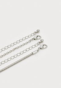 Sølv metal kæde med tre sektioner: kædelink, glatte rundede links og en fleksibel slange kæde, alle med drejelåse.