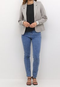Lys grå fitted blazer med en enkelt knap, parret med en sort top, blå skinny jeans og sorte strop sandaler. Glat stof og skræddersyet design.