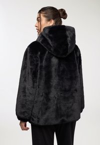 Giacca in pelliccia sintetica nera con cappuccio, caratterizzata da una consistenza morbida, una forma voluminosa e spalle cadenti, vista da dietro.