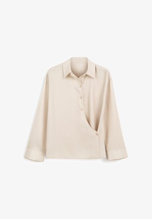 Beżowa koszula z długim rękawem z szpiczastym kołnierzykiem, asymetrycznym zapięciem na guziki zakrzywiającym się od klatki piersiowej do talii oraz szerokimi mankietami.