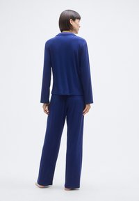 Σετ άνετης φορεσιάς σε ναυτικό μπλε χρώμα, που περιλαμβάνει μακρυμάνικο τοπ με γιακά και φαρδιά παντελόνια, κατασκευασμένο από απαλό, λείο ύφασμα. Απλός σχεδιασμός.