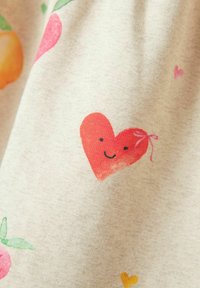 Koszula z krótkim rękawem wykonana z tkaniny w beżowym tle z kolorowymi wzorami owoców i uśmiechniętych serc w odcieniach różu i pomarańczy. Miękka w dotyku.