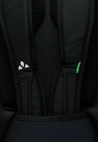 Close-up van een zwarte rugzak met gewatteerde, mesh rugondersteuning, verstelbare schouderbanden en witte en groene logo-accenten. Textuurdetails van de stof zijn zichtbaar.