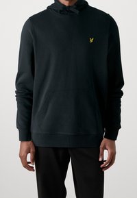 Sudadera con capucha negra de algodón, con un bolsillo frontal, puños acanalados y un pequeño logo amarillo en el pecho. Textura suave con un ajuste relajado.