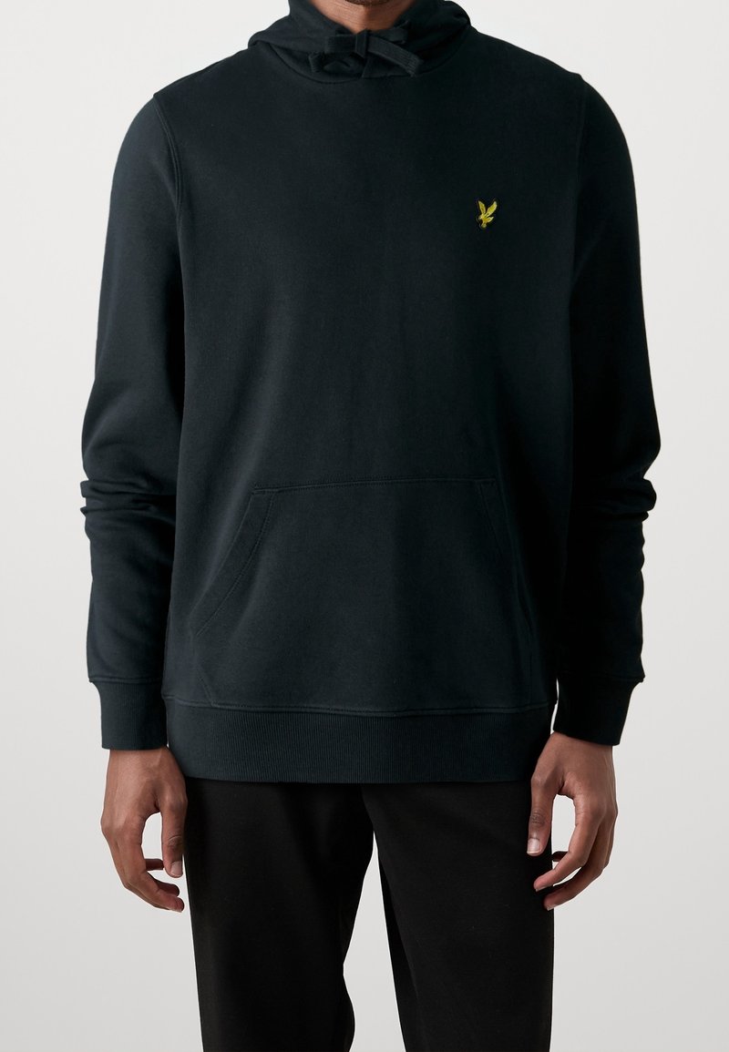 Sudadera con capucha negra de algodón, con un bolsillo frontal, puños acanalados y un pequeño logo amarillo en el pecho. Textura suave con un ajuste relajado.