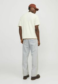 Valge puuvillane lühikeste varrukatega T-särk, mille alla on kihiline pruun särk, koos helesiniste sirgete joontega teksade ja tumedate pruunide kingadega, vaadatuna tagant.