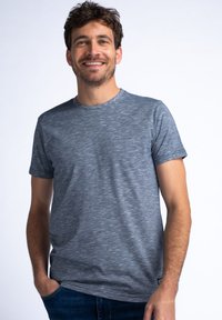 Šedé tričko s krátkým rukávem a jemnou heather texturou, kulatým výstřihem a plochými švy. Nosené s modrými džíny, které ukazují ležérní střih.