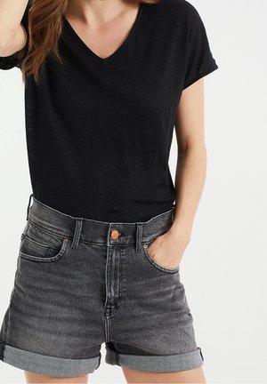 T-shirt nera a V abbinata a pantaloni corti di jeans grigi a vita alta. I pantaloni corti presentano un orlo arrotolato e tasche, con bottoni in ottone.