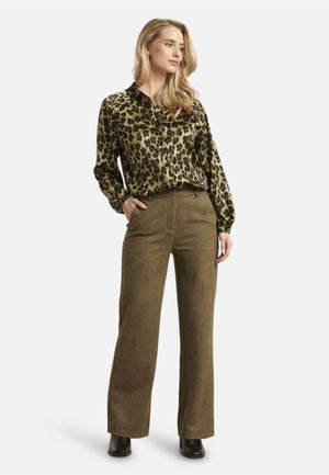 Leopard-print silk blouse with a collar, paired with wide-leg olive green suede pants. Model stands in black heeled boots.