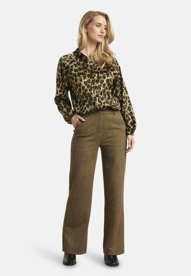 Leopard-print silk blouse with a collar, paired with wide-leg olive green suede pants. Model stands in black heeled boots.