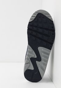 Suela de zapatilla Nike con una base de goma negra texturizada y una entresuela gris, que presenta un patrón de olas y detalles que no marcan.