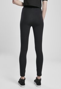 Čierne legíny s priliehavým strihom, vyrobené z elastického materiálu, s vysokým pásom a dĺžkou po členky. Nosia sa s čiernymi teniskami.