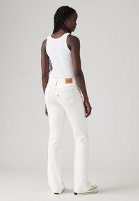 Hvite slengjeans med kontraststing, baklommer og et merketikett i midjen. Bært med en tettsittende hvit topp.