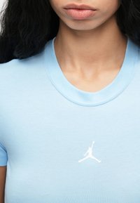 Κοντινό πλάνο ενός ατόμου που φοράει ένα ανοιχτό μπλε μπλουζάκι με ένα μικρό λευκό λογότυπο μπασκετμπολίστα στο στήθος.