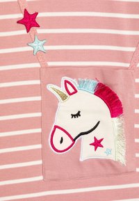 Różowo-biały materiał w paski z naszywką jednorożca z złotym rogiem, kolorową grzywą i dwoma wyhaftowanymi gwiazdkami.