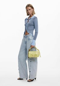 Hellblauer gerippter Cardigan mit Kragen, kombiniert mit übergroßen Jeans aus hellem Denim mit Knopfdetails. Kombiniert mit einer gelben Umhängetasche.