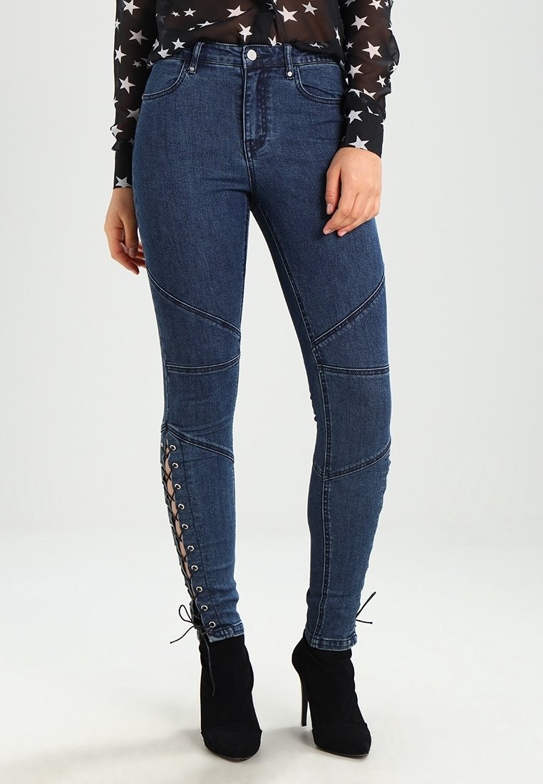 Tmavě modré džíny s přiléhavým střihem, které mají diagonální švy a šněrovací detaily po stranách spodní části nohavic.