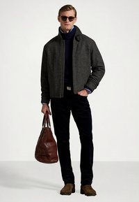 Pilka vilnonė striukė su stovinčiu apykakliu, mėlynos spalvos golfas, tamsios kelnės, ruda odinė rankinė ir rudi batai. Modelis dėvi akinius nuo saulės.