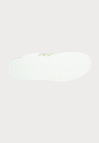 White athletic shoe sole with a textured pattern, featuring a distinctive logo in a soft green accent. Smooth and flexible material.