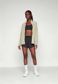 Hele roheline jakk musta spordirinnahoidja peal, koos mustade lühikestega. Valged spordisokid ja stiilsed valged jalanõud lõpetavad riietuse.