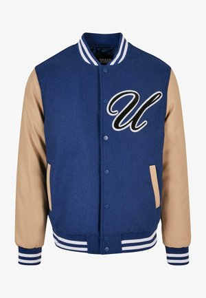 Tumedat sinine ülikooli jope beežide varrukatega, millel on esiletõstetud tikandiga "U" logo ning triibulised soonikvarrukad ja -vöö.