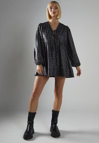 Schwarzes Leopardenmuster-Kleid mit V-Ausschnitt, Zugbanddetails an der Brust und langen Puffärmeln, kombiniert mit schwarzen Knöchelstiefeln.