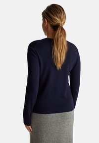 Námorně modrý svetr z jemné tkaniny, s kulatým výstřihem a žebrovanými manžetami. Zobrazen ze zadní strany s hladkou strukturou.
