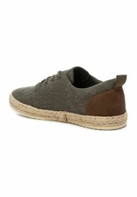 Espadrilles de lona gris con detalles en cuero marrón, puntera redonda, diseño con cordones y suela de yute trenzada. Estilo minimalista y casual.