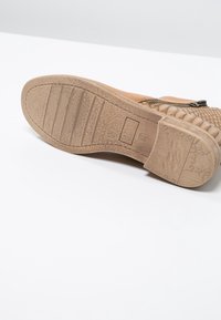 Tan väri nahkakenkien pohja, jossa on teksturoitu kumia ja erottuvat pito-kuviot sekä vahvistava kanta. Mukana muotoiltu brändäysdetail.