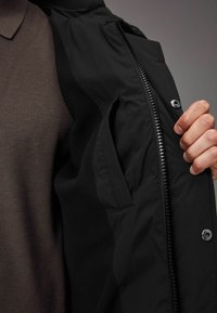 Chaqueta negra con forro gris, que presenta un cierre de cremallera y botón a presión, textura suave y un bolsillo oculto en su interior.