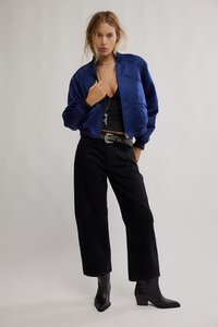 Modrý saténový bomber s žebrovanými manžetami, kombinovaný s černými vysokým pasem z džínoviny a černými kotníkovými botami, doplněný řetězovým opaskem.