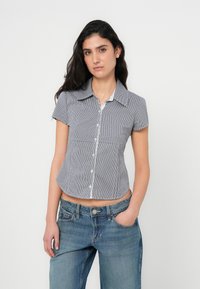 Μπλε και λευκό πουκάμισο με κοντά μανίκια και καρώ σχέδιο, με μυτερό γιακά, κουμπιά στο μπροστινό μέρος και εφαρμοστή γραμμή. Φοριέται με τζιν ψηλόμεσο.