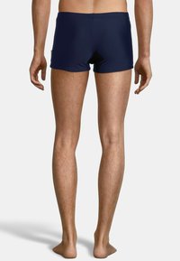 Shorts de bain navy au design ajusté, fabriqués en matériau extensible, présentant une texture lisse et un style minimaliste.