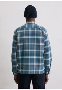 Niebieska koszula w kratę z białym i jasnoniebieskim wzorem w kratkę, z długimi rękawami, zapinanymi mankietami i kołnierzem, noszona z granatową dzianinową czapką beanie.