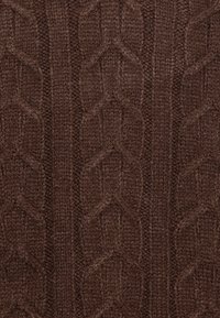 Tissu tricoté marron avec un motif en câble texturé, des mailles en relief formant un motif répétitif. Texture douce et chaleur apparente.